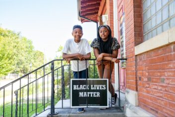 Grace & Yosiyah are siblings standing on their deck with a Black Lives Matter sign.