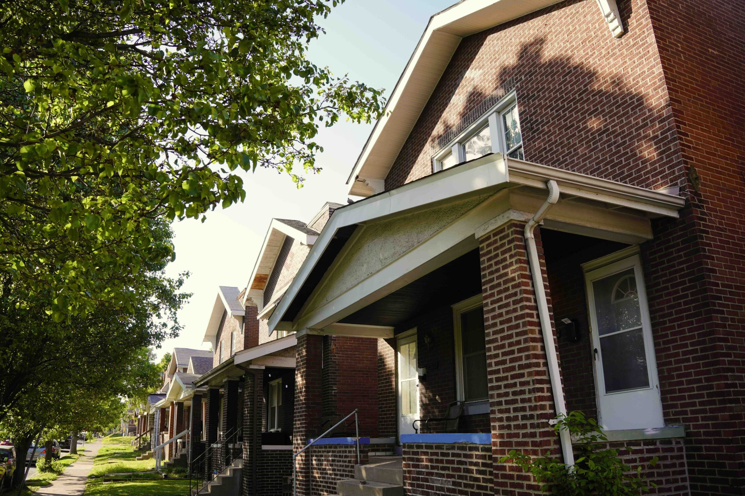 Row of houses in Dutchtown with red bricks and porches. On the left are green trees.