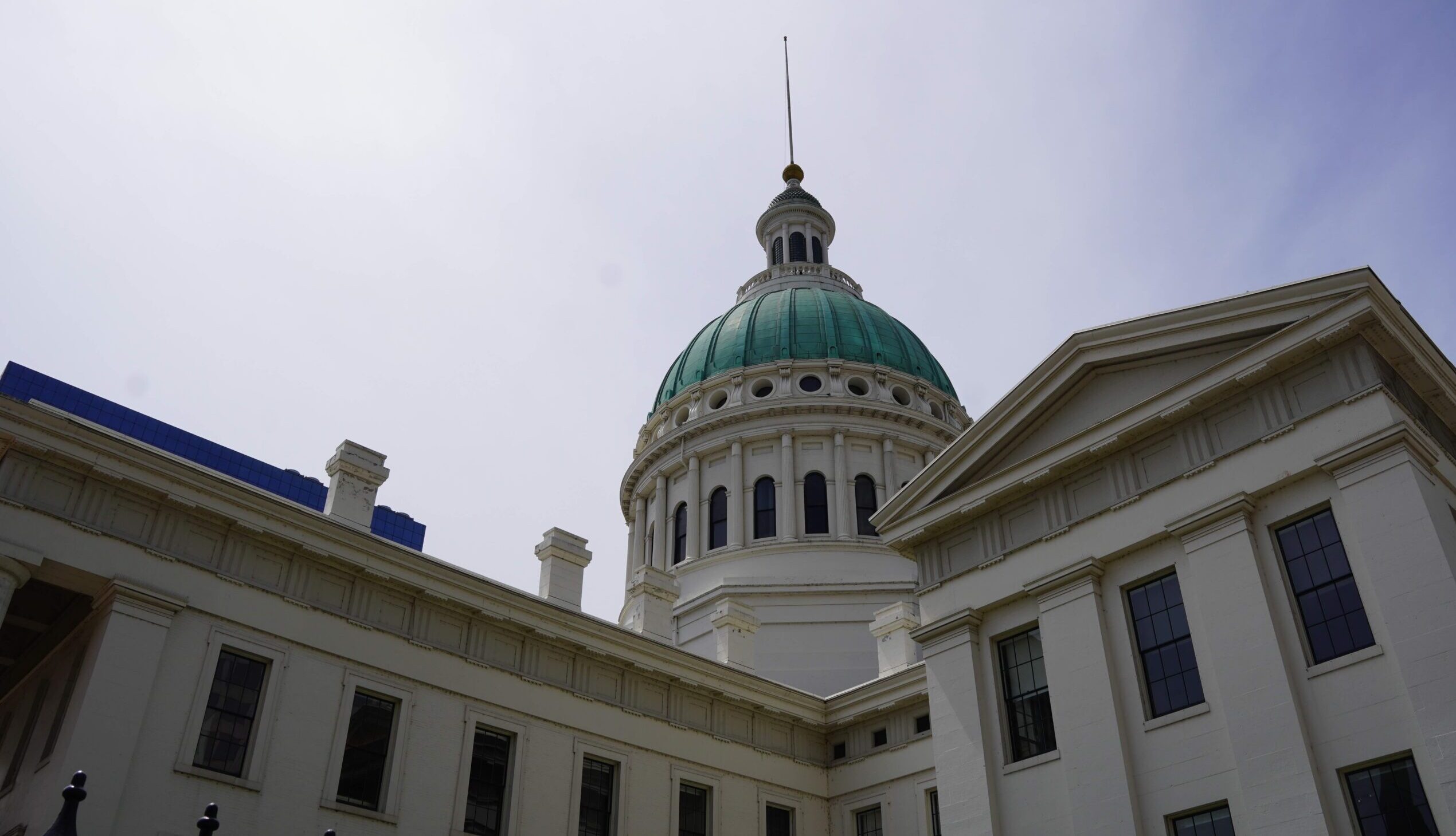 A view of the top of the Old Courthouse with the dome peaking out from the middle and the corners of the buildings on either side. The sky is above.