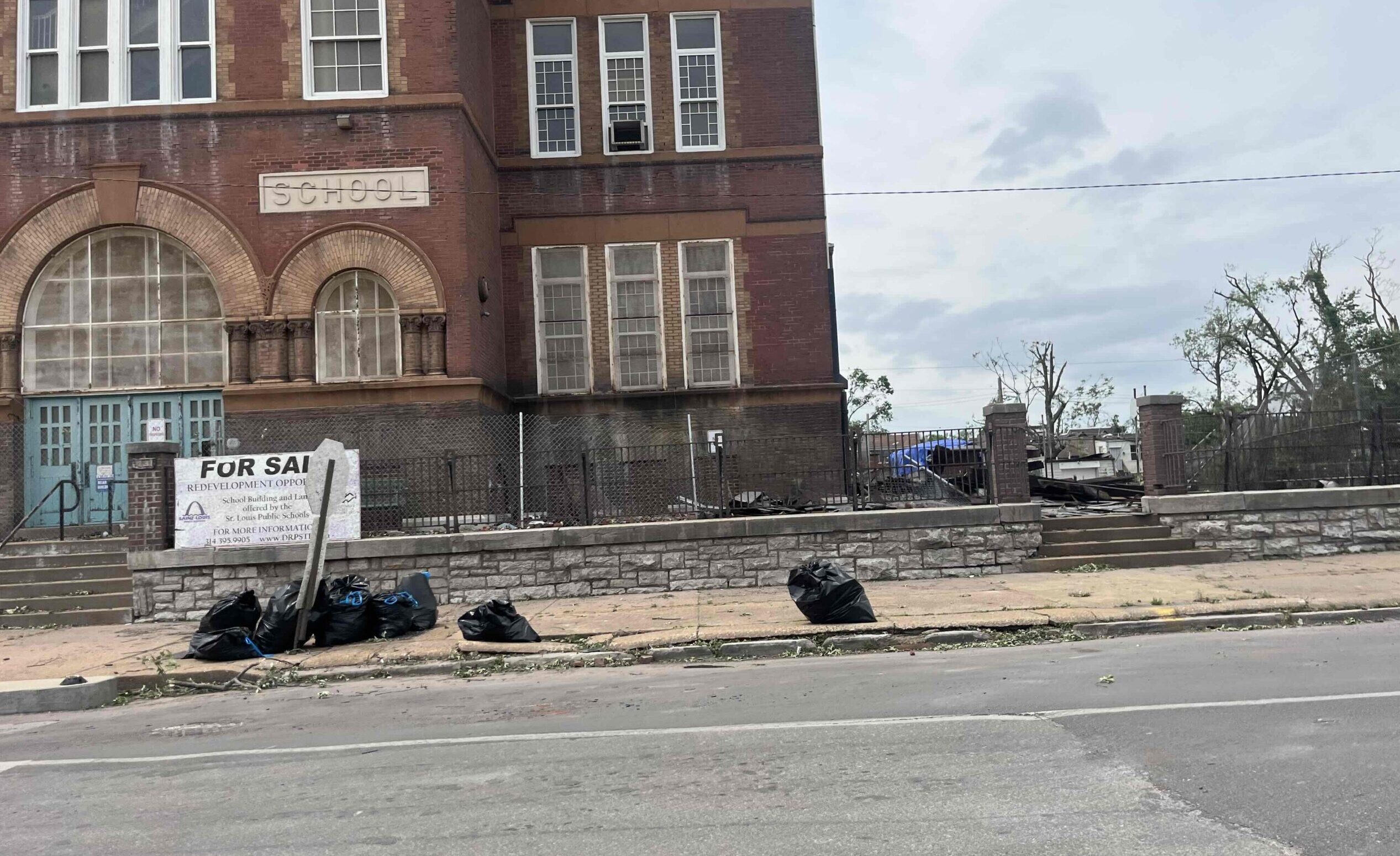 A school that is for sale with debris in heavy duty trash bags piled up on the sidewalk.